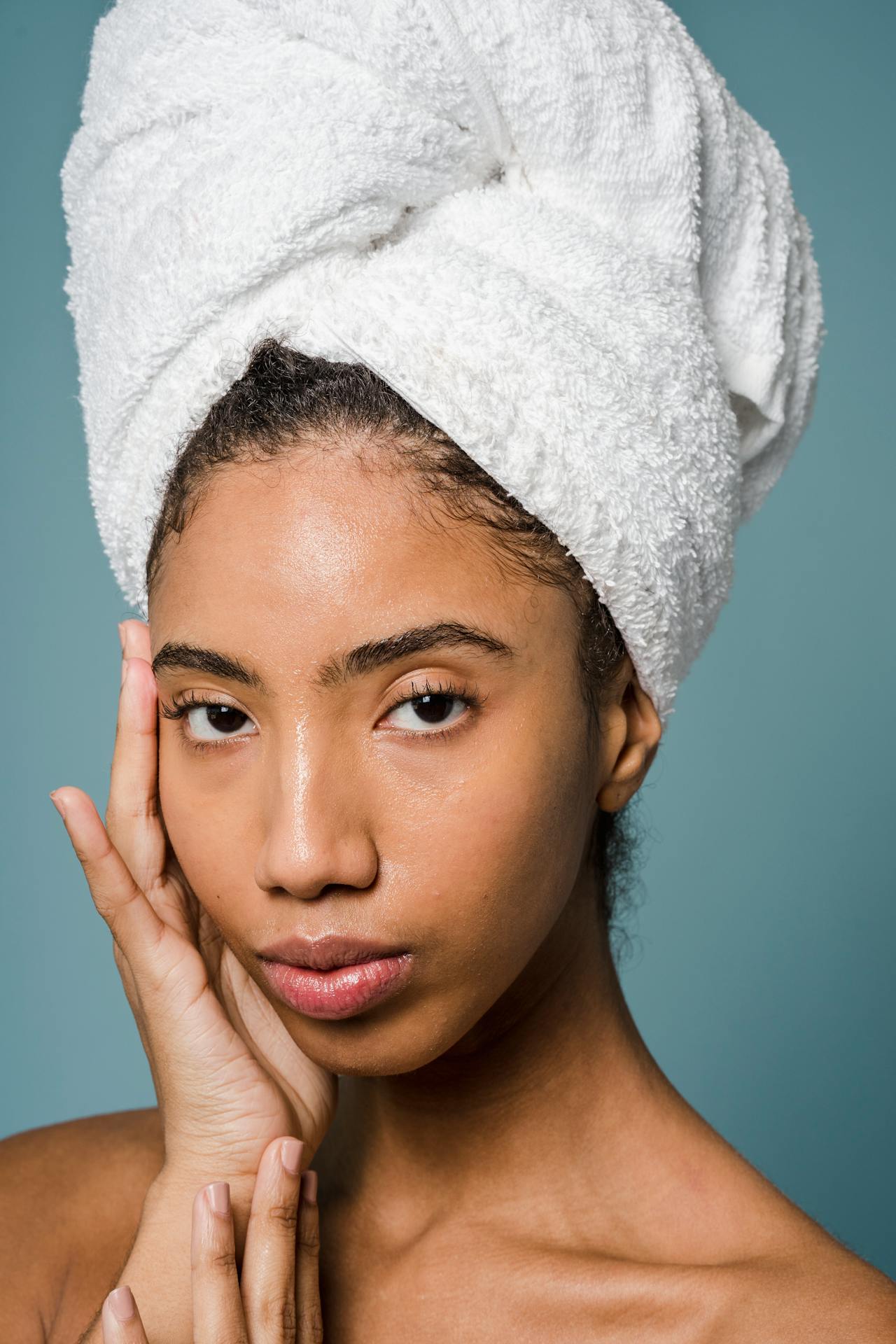 Graceful young ethnic woman applying cream on face after shower