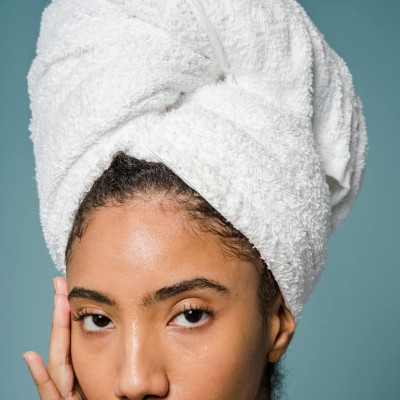 Graceful young ethnic woman applying cream on face after shower