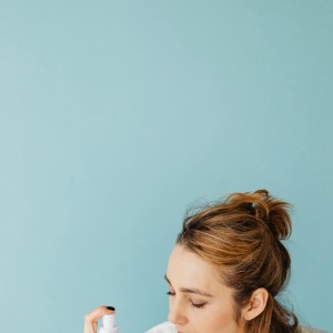 A Woman Spraying on Her Face with Her Eyes Closed