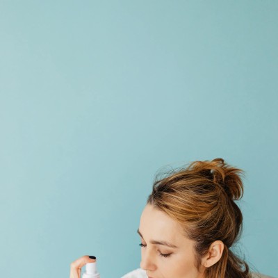 A Woman Spraying on Her Face with Her Eyes Closed