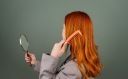 Red-haired woman brushing hair with mirror